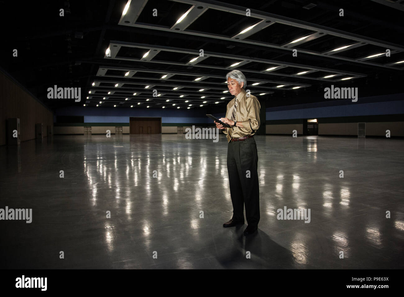 An Asian businessman standing in a dimly lit and dark exhibition area in a convention center. Stock Photo