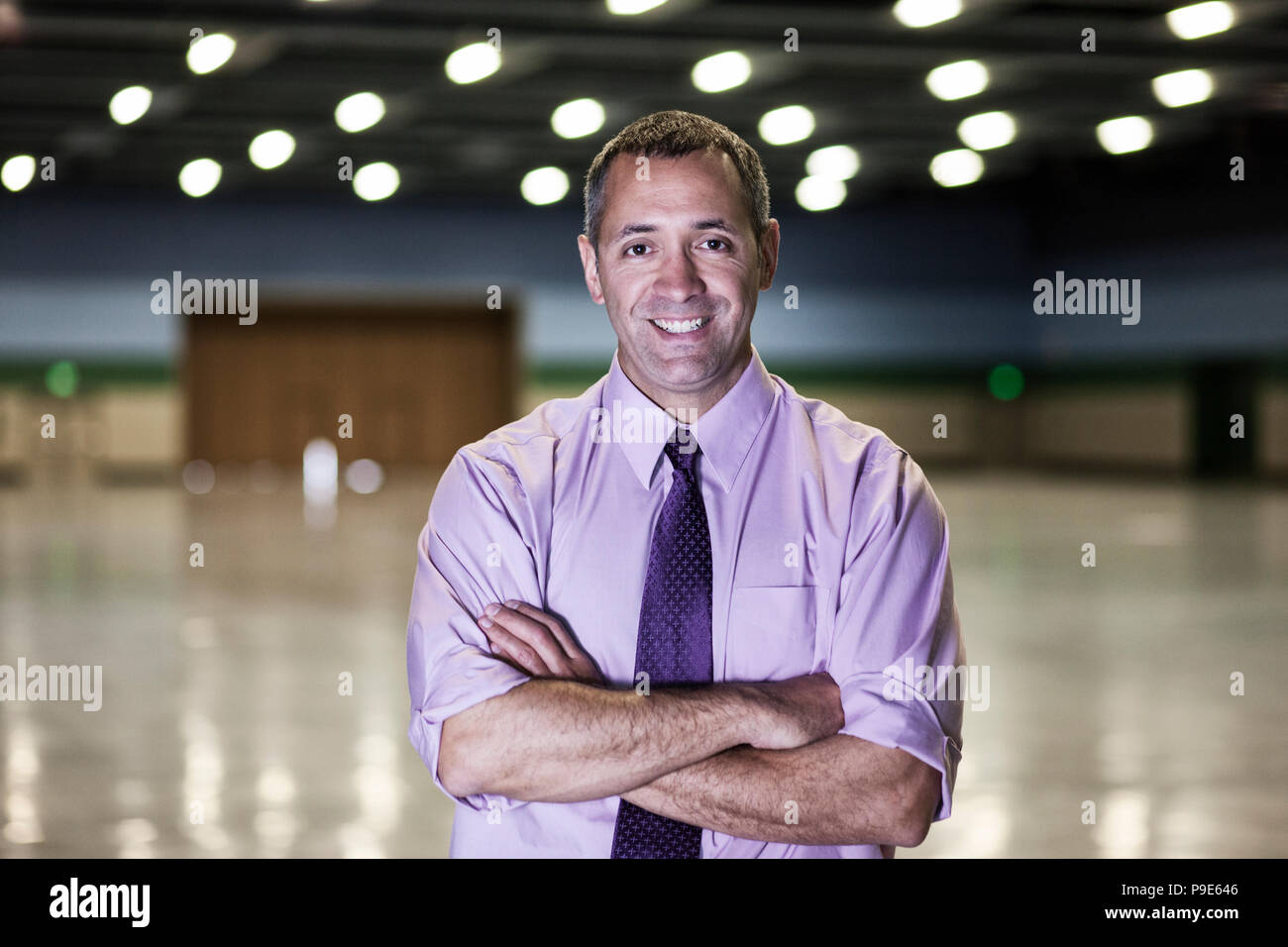 A Caucasian businessman standing in a dimly lit and dark exhibition area in a convention center. Stock Photo