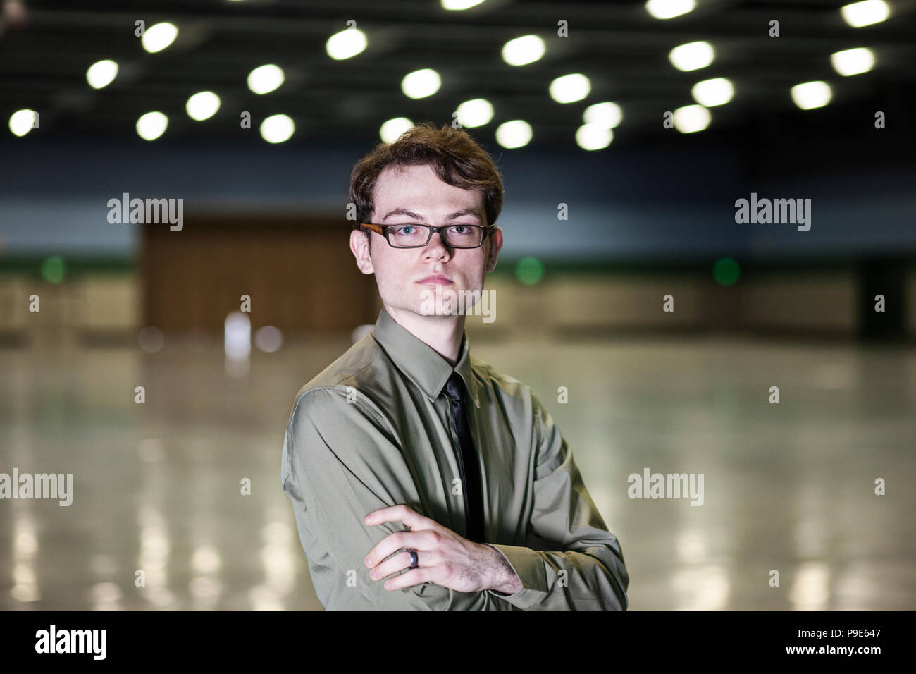 A young hip businessman standing in a dimly lit and dark exhibition area in a convention center. Stock Photo