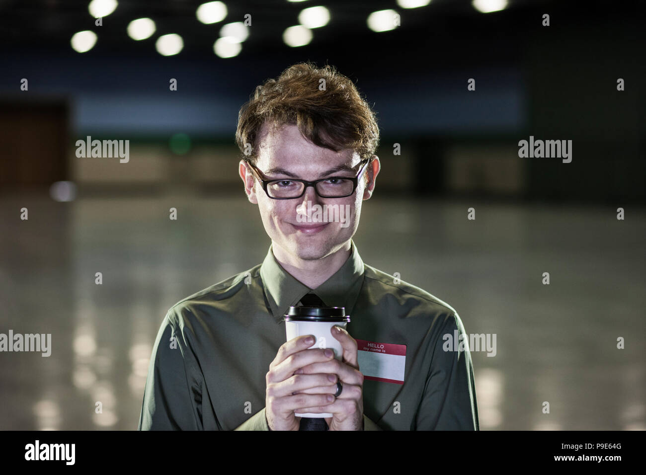 A young hip businessman standing in a dimly lit and dark exhibition area in a convention center. Stock Photo
