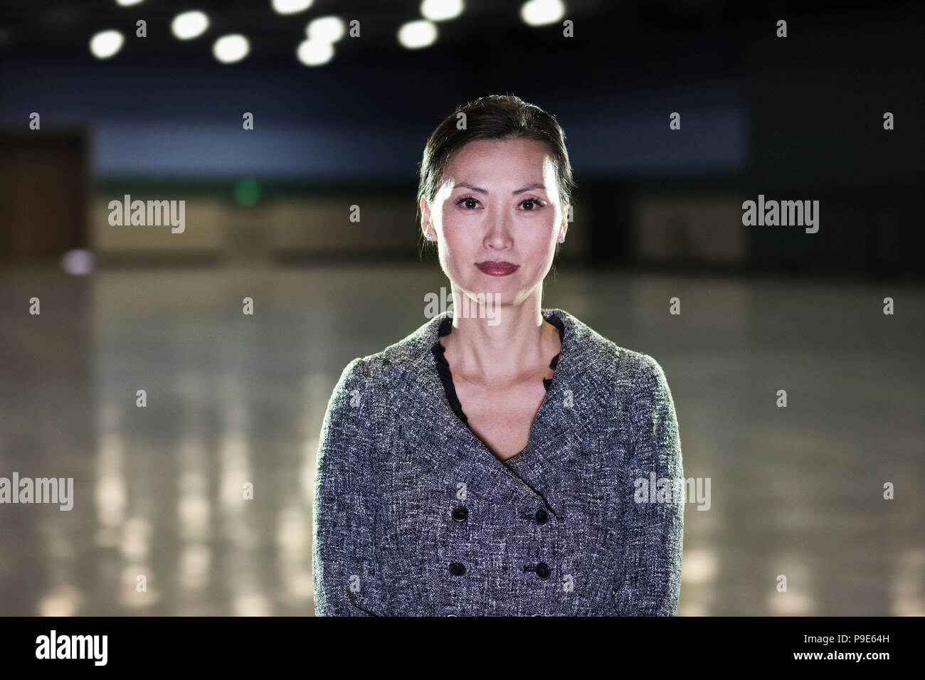 An Asian businesswoman  standing in a dimly lit and dark exhibition area in a convention center. Stock Photo