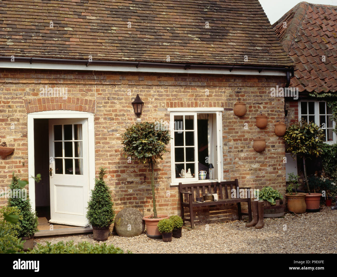 Open half-glazed white door in cottage extension with bench below window onto gravel courtyard Stock Photo