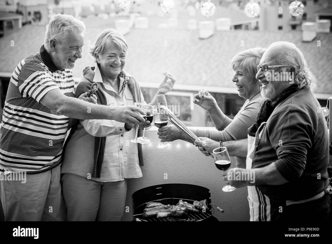 senior adult people group in leisure activity doing barbeque bbq on the rooftop terrace at home with mountain view. meal and wine for two men and two  Stock Photo