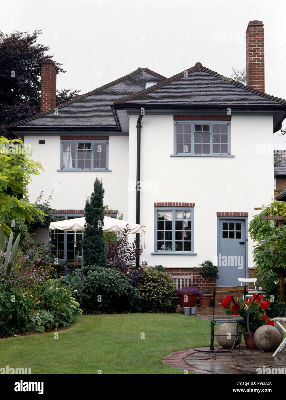 Exterior of a white thirties detached house with grey paintwork and a well-stocked garden Stock Photo