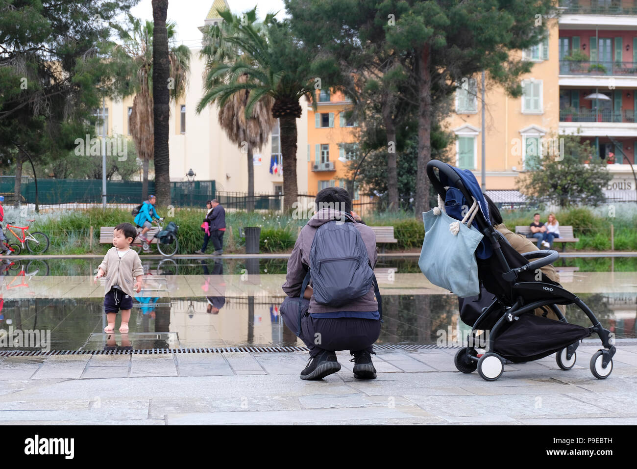 Nice, France. Father watching his toddler playing in the Miroir d’Eau Stock Photo