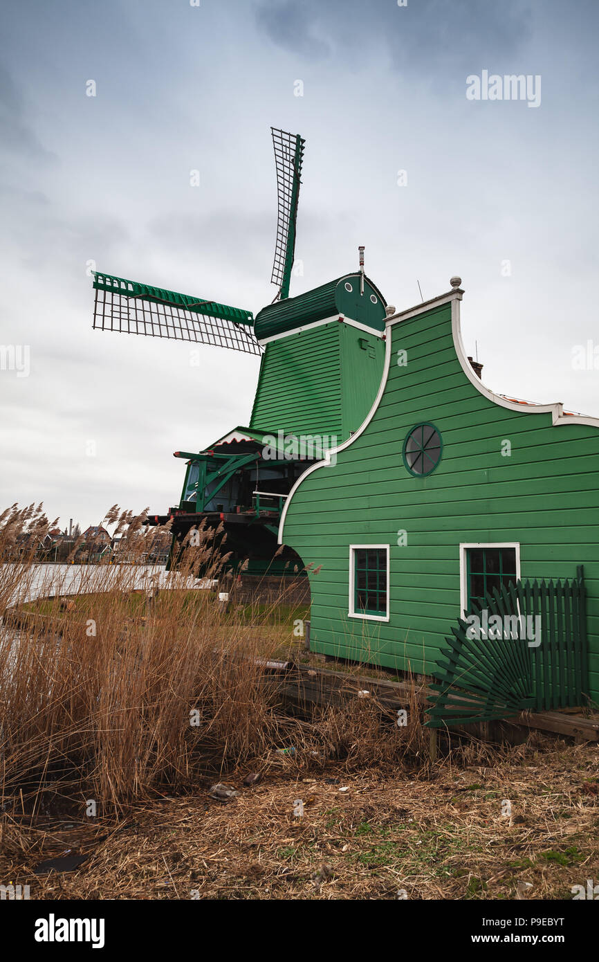 Windmill and green barn on Zaan river coast, Zaanse Schans town, popular tourist attractions of the Netherlands. Suburb of Amsterdam Stock Photo