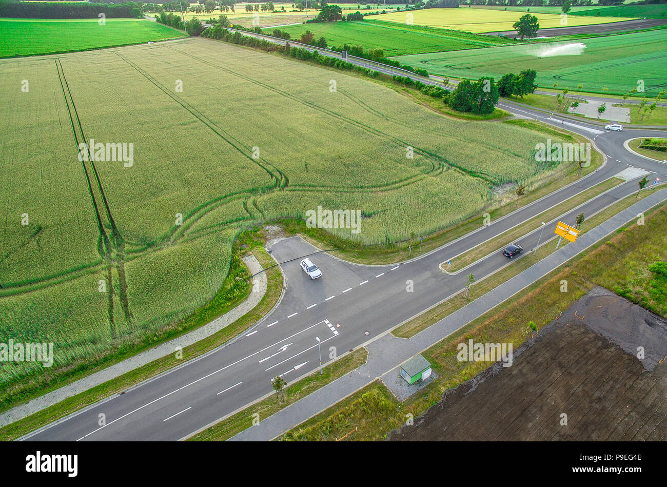 Aerial view of a road with signs and guidelines for traffic between a new development area for an industrial estate and an arable area with green whea Stock Photo