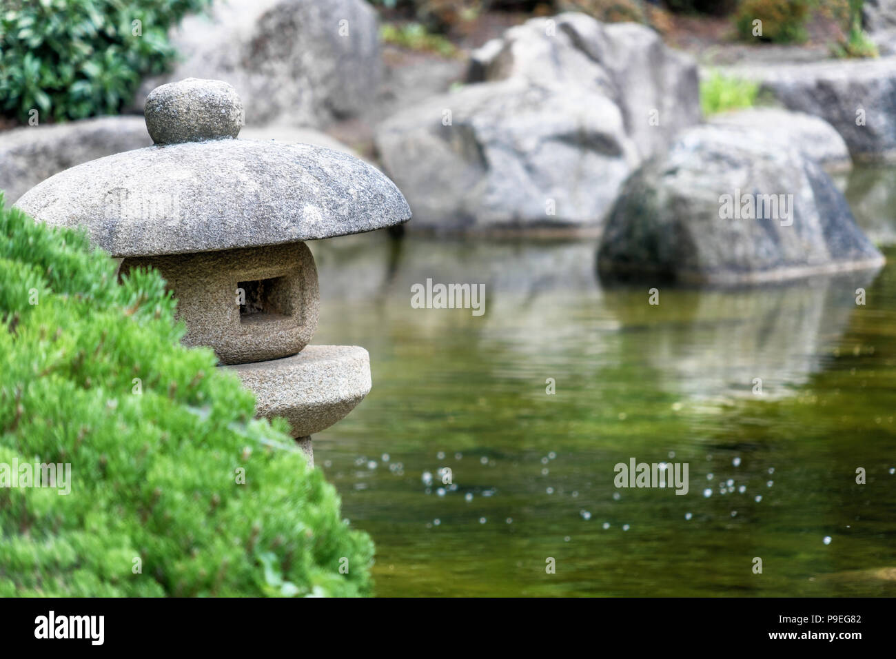 Pond in a Japanese garden with a traditional stone lantern in the foreground, low depth of field Stock Photo