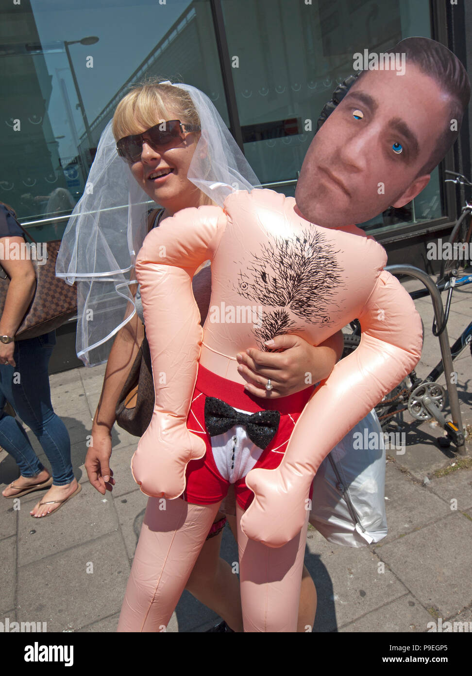 A future bride on a hen do in Brighton holds an inflatable doll with a mask of her betrothed Stock Photo