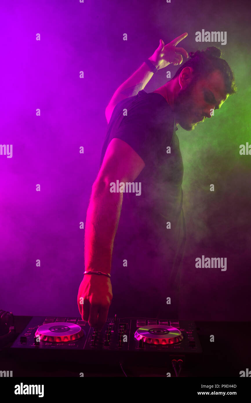 Attractive young DJ playing on turntables with color light effects