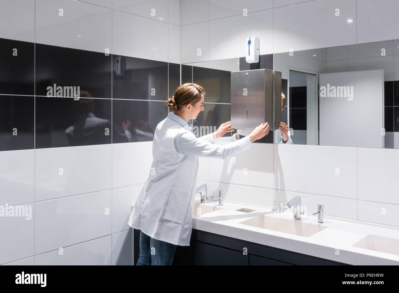 Cleaning woman refilling paper towels in public toilet  Stock Photo