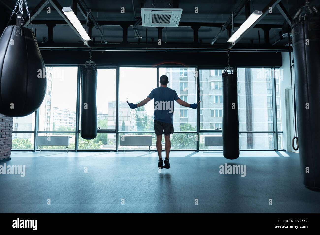 Black-haired athlete jumping rope standing near window Stock Photo