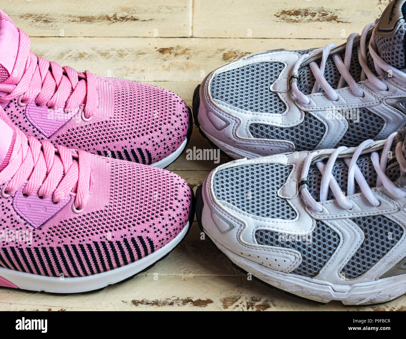 On the wooden surface is a pair of pink women's sneakers and a pair of ...