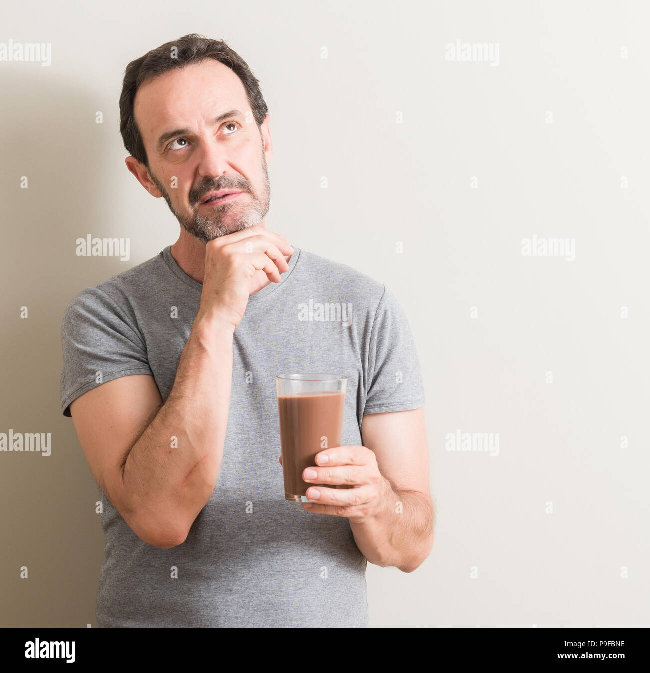 Senior man drinking chocolate milk shake serious face thinking about