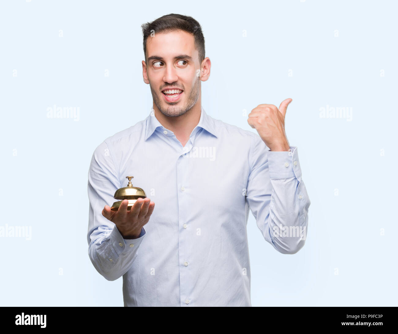 Handsome young man holding hotel ring bell pointing with hand and ...