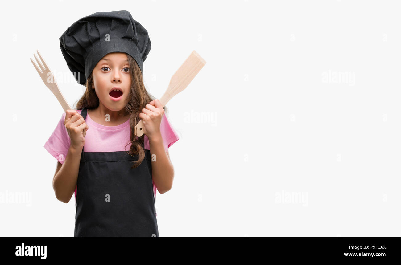 Brunette hispanic girl wearing cook uniform scared in shock with a surprise face, afraid and excited with fear expression Stock Photo