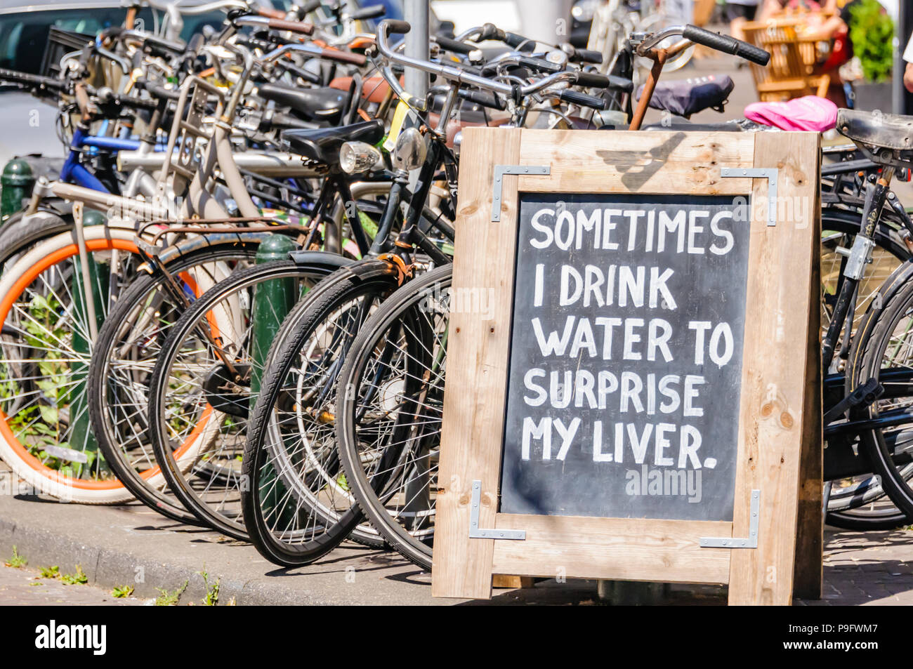 Sign beside some parked bicycles saying 'Sometimes I drink water to surprise my liver', Stock Photo