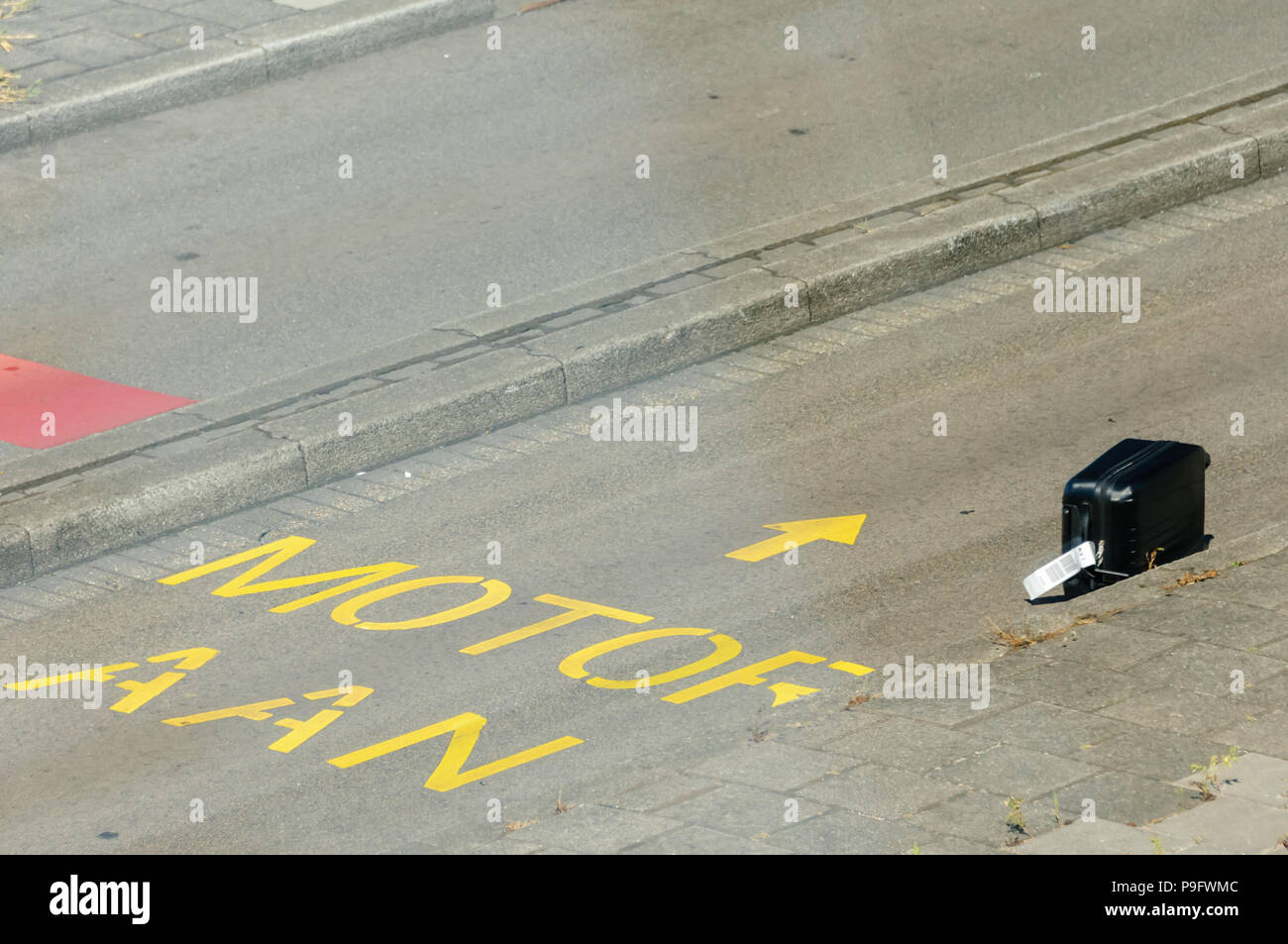 Passenger luggage suitcase lies on an airport road after falling off a baggage truck, will be lost luggage. Stock Photo
