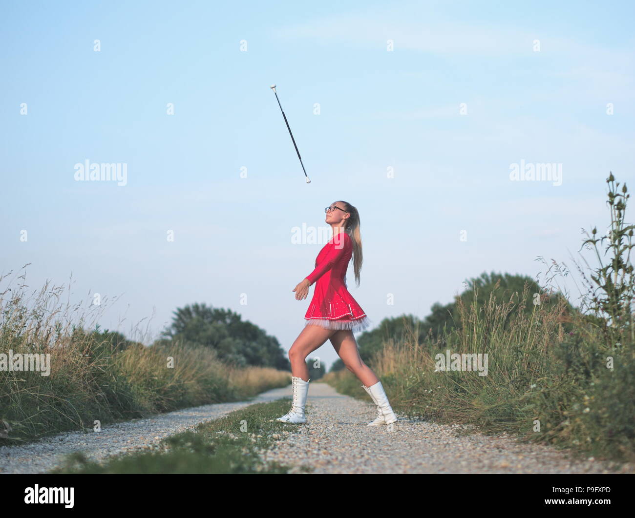 Bespectacled Blonde Teen Majorette Girl Twirling Baton Outdoors in Red Dress Stock Photo