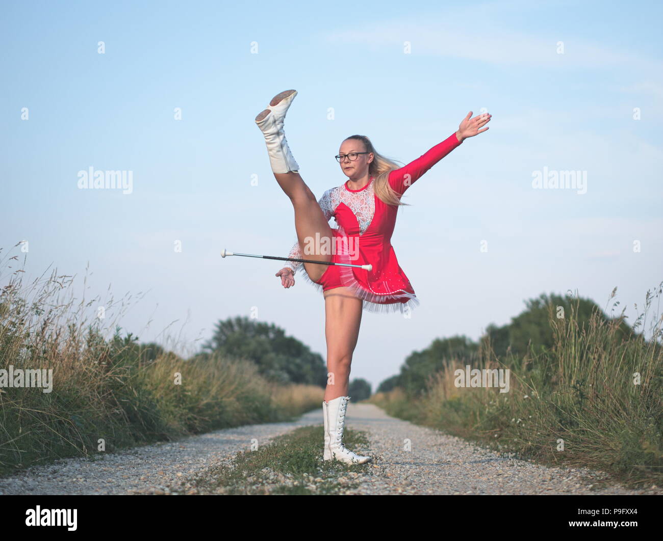 Bespectacled Blonde Teen Majorette Girl Twirling Baton Outdoors in Red Dress Stock Photo