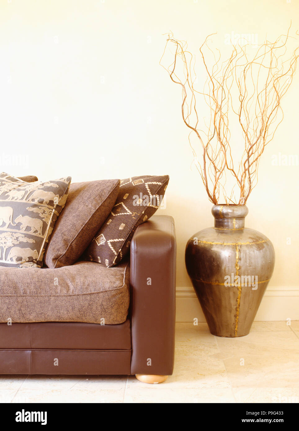 Ethnic-patterned cushions on brown leather sofa beside branches in Moroccan pot Stock Photo