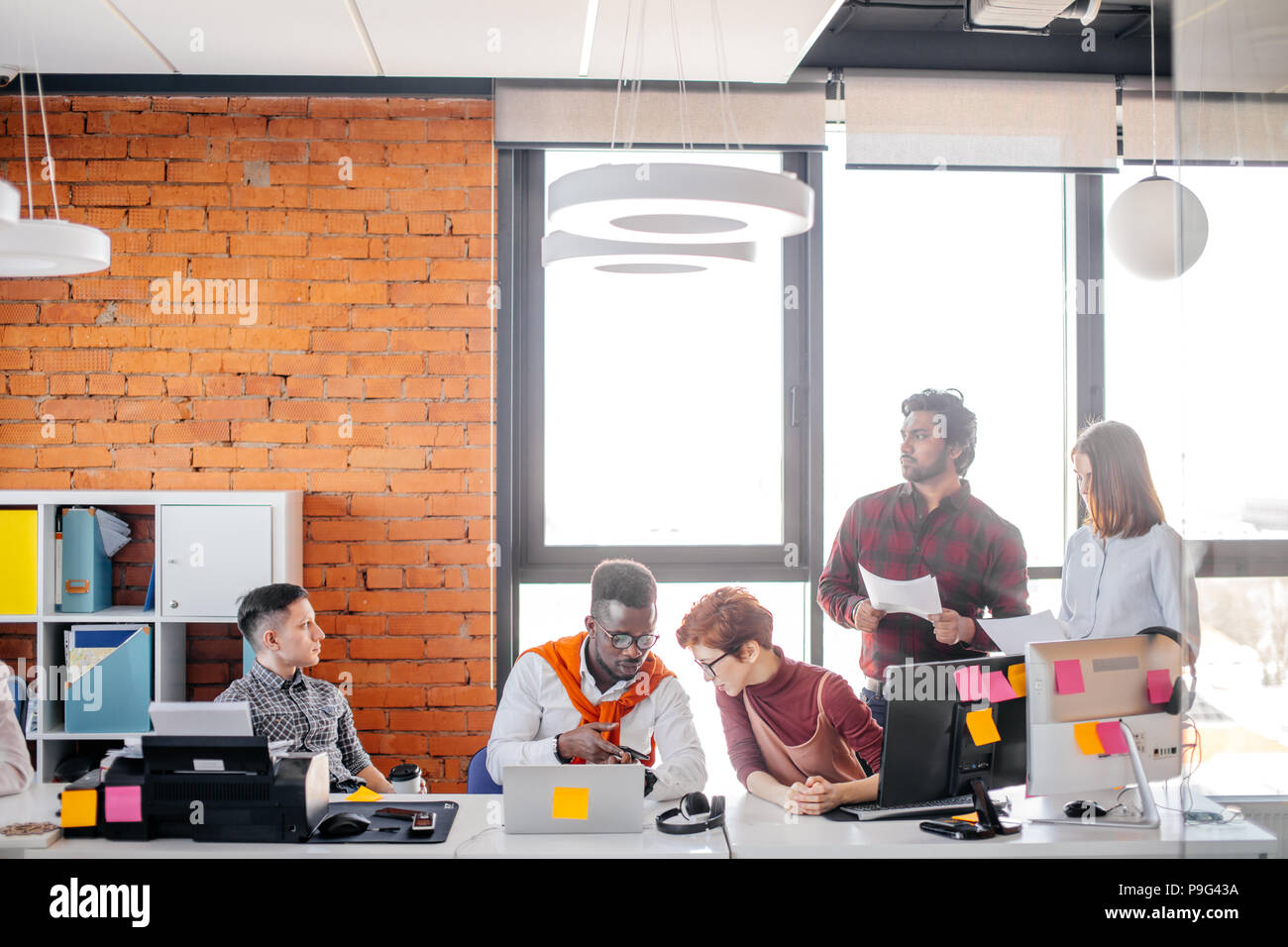 thoughtful Indian guy holding paper and looking away in the office with colleagues Stock Photo