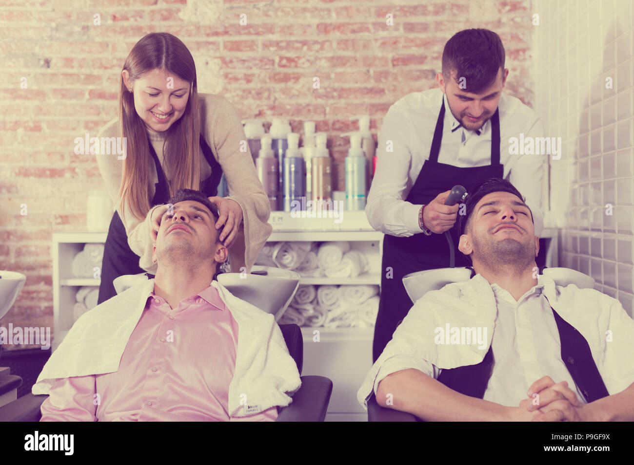 Men Leaning Heads On Sink And Relaxing While Hairdressers Washing