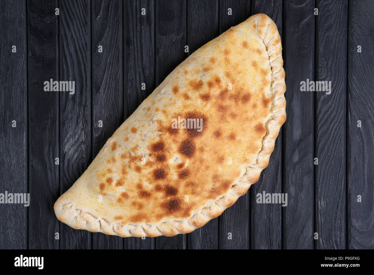 Fresh baked pizza calzone on dark wooden table, top view. Stock Photo