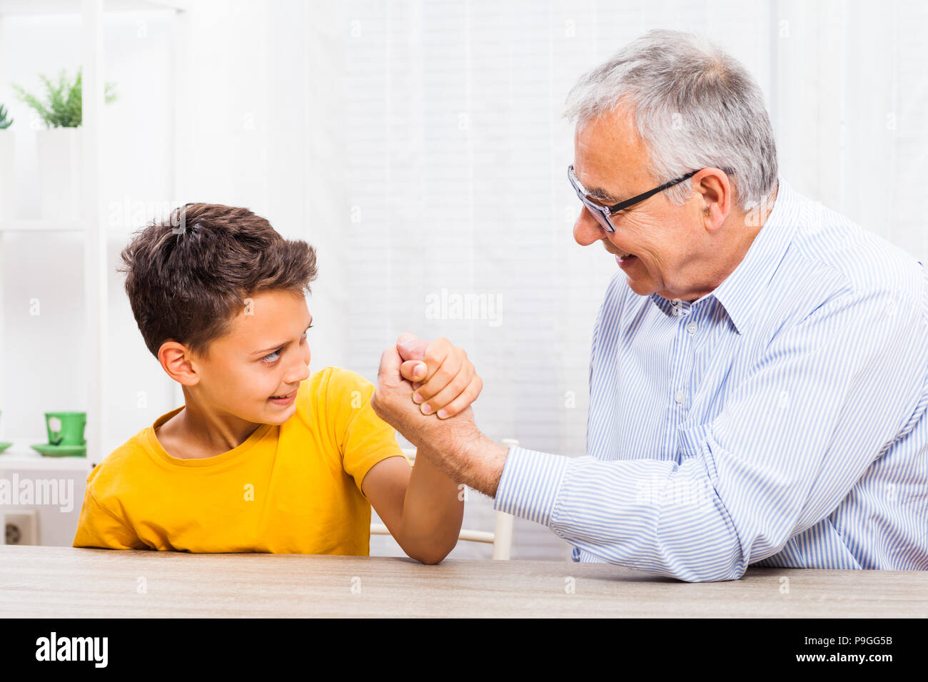 Grandfather and grandson arm wrestle at home. Stock Photo