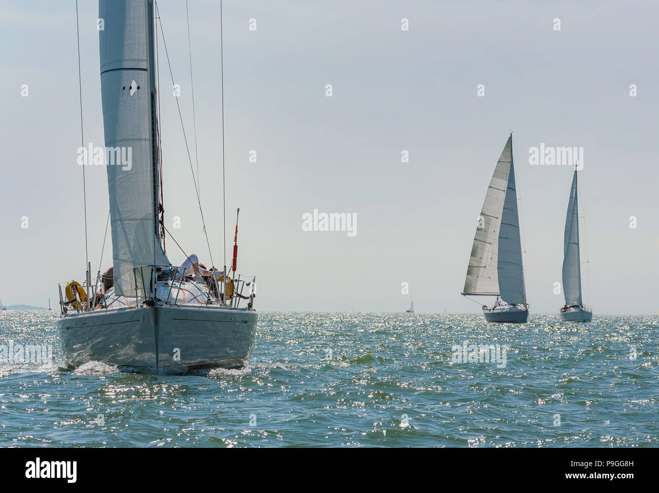 Three beautiful white yachts, sailboats or sail boats sailing at sea on a calm, bright sunny day Stock Photo