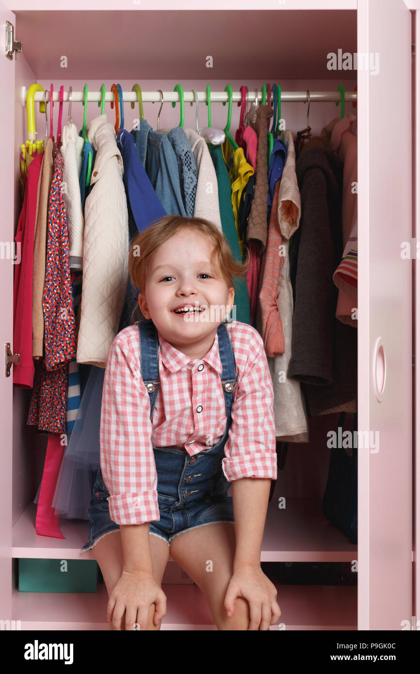A little girl is sitting in a wardrobe with a children's department