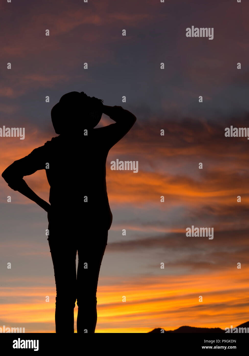 Woman in trousers with hat silhouette looking at sunset, sunrise. Background with copyspace. Stock Photo