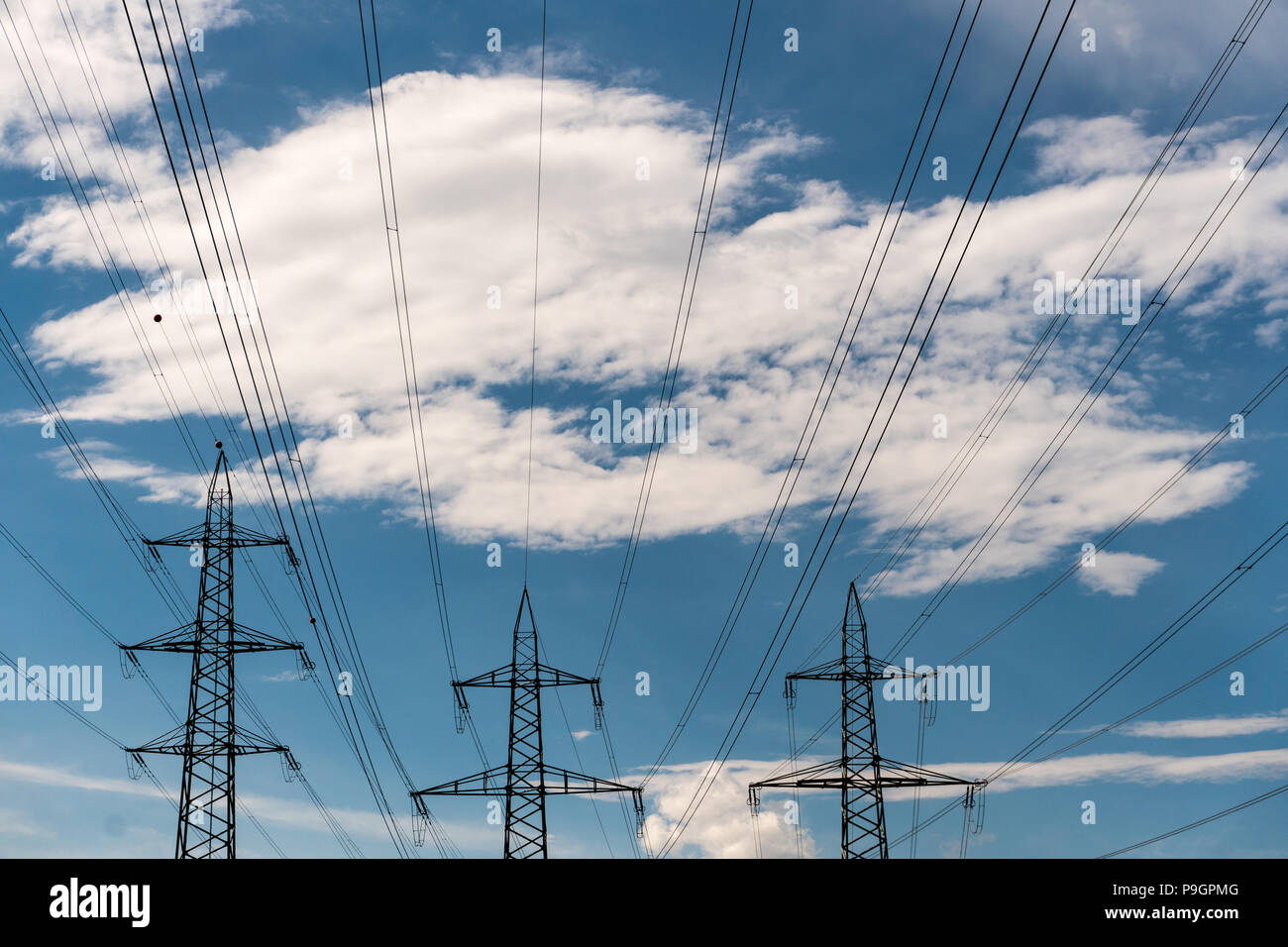 power lines and pylons in silhouette against a blue sky with white ...