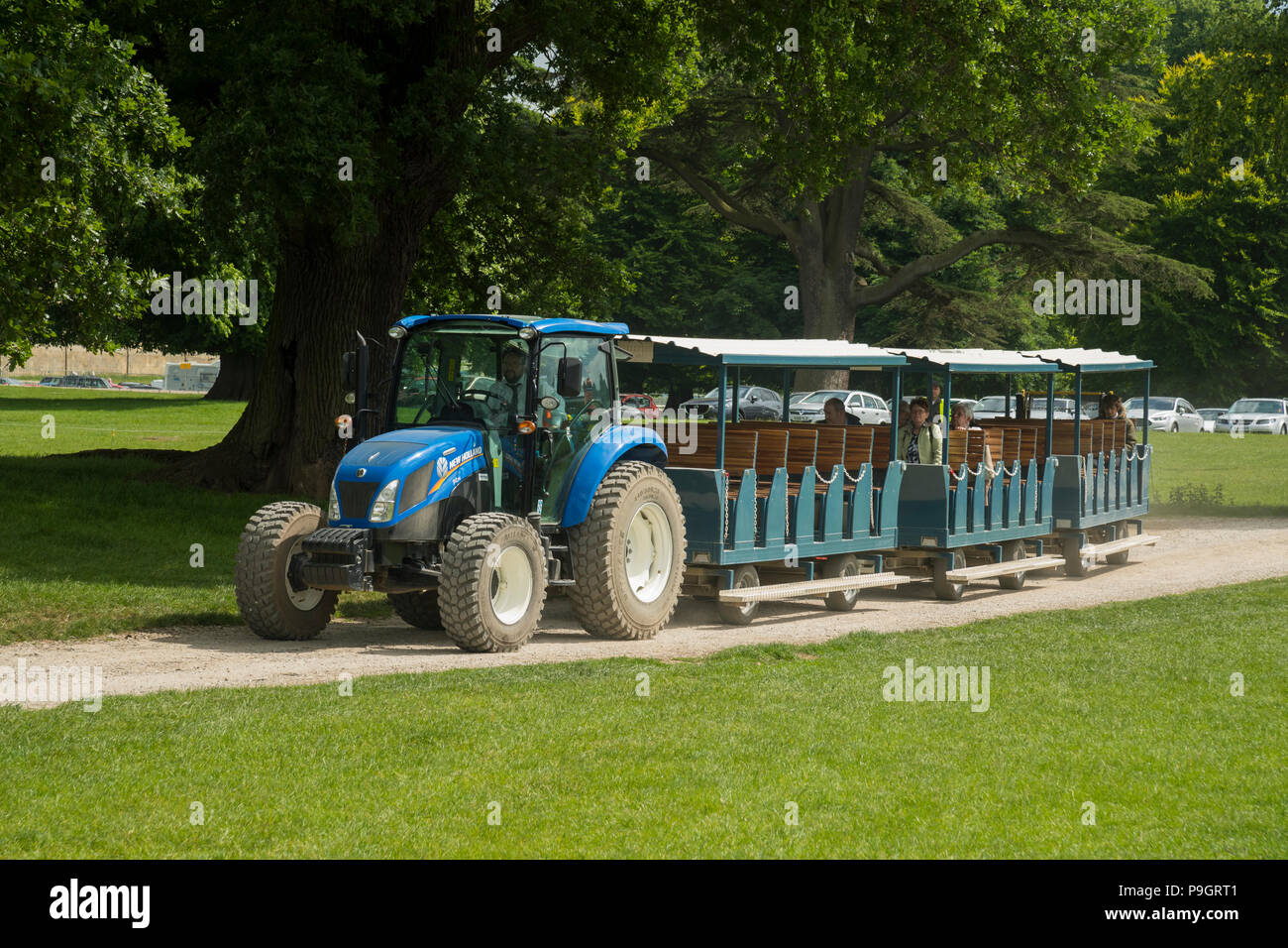 Visitors arriving at showground, transported from car park in carriages pulled by blue tractor - RHS Chatsworth Flower Show, Derbyshire, England, UK. Stock Photo