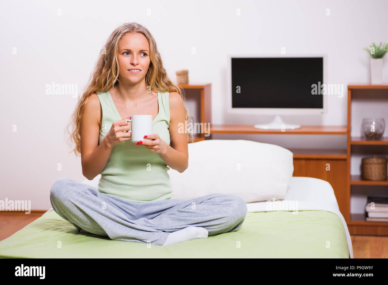 Young woman is sitting in her bed and drinking tea. Stock Photo