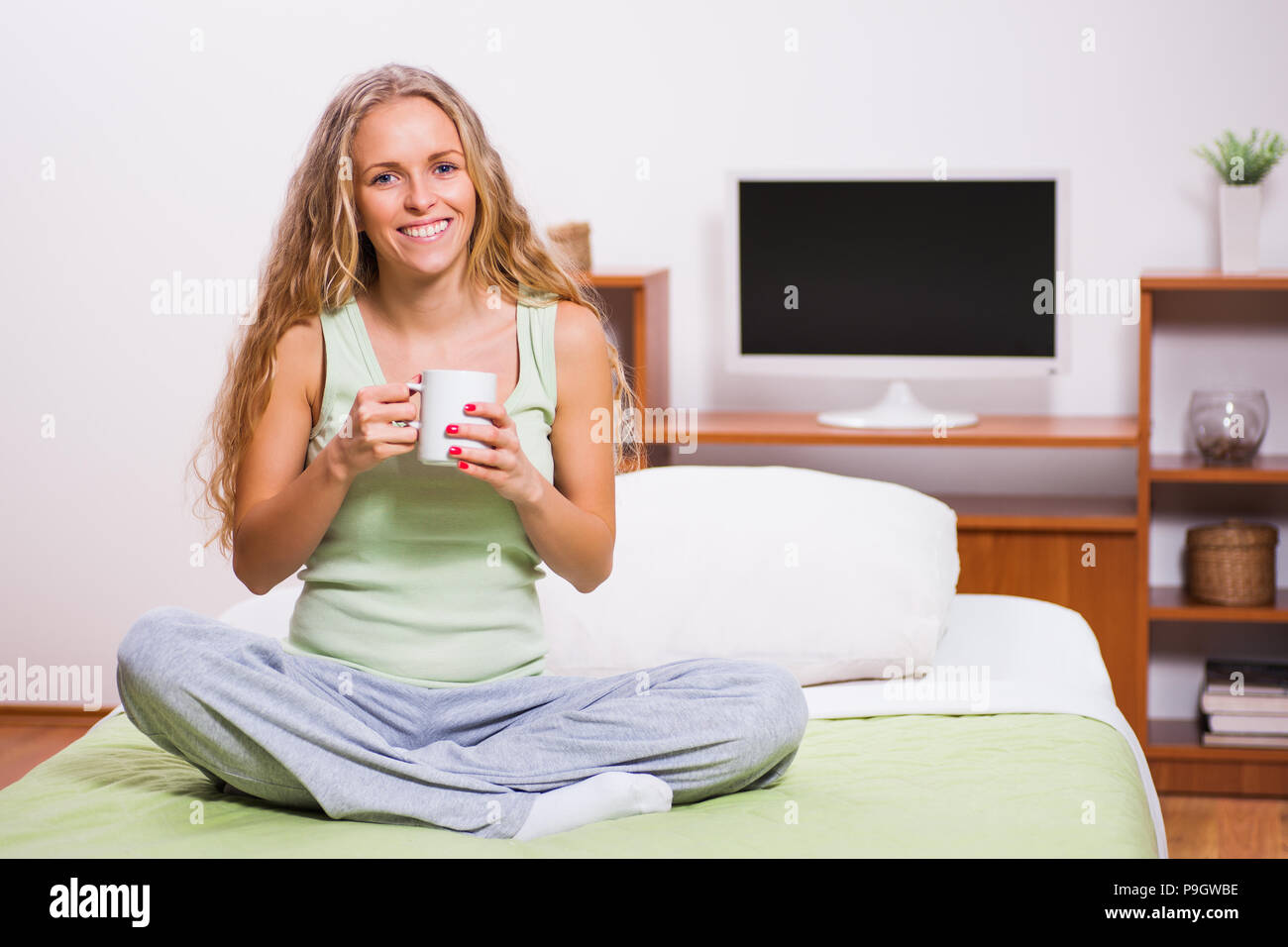 Young woman is sitting in her bed and drinking tea. Stock Photo