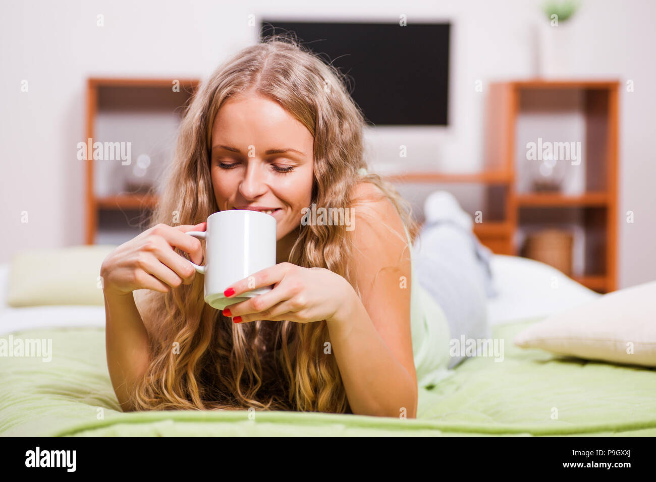 Young woman is lying in bed and drinking tea. Stock Photo