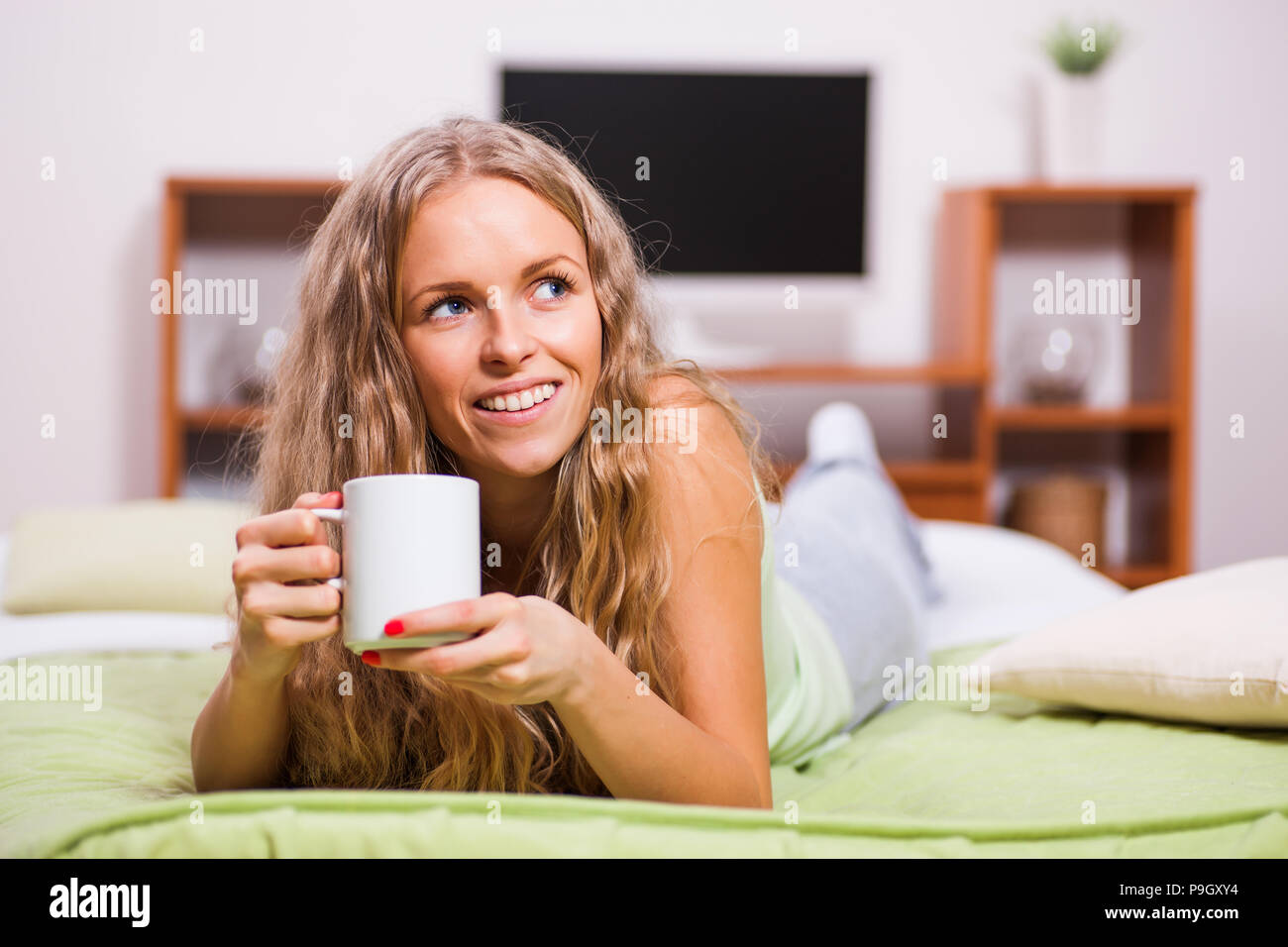 Young woman is lying in bed and drinking tea. Stock Photo