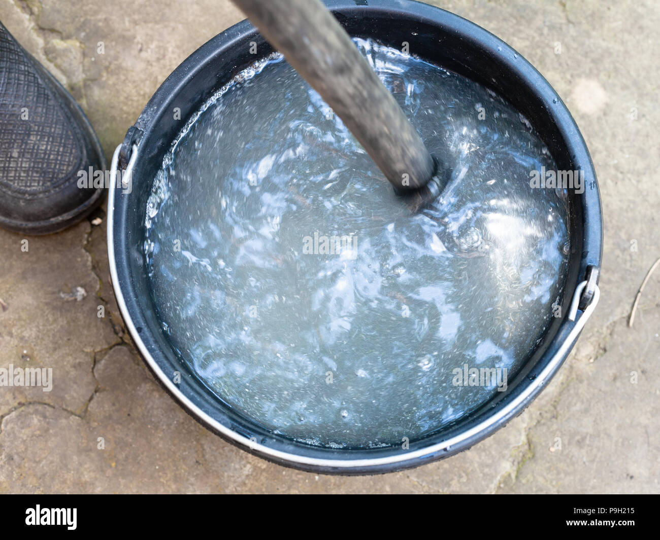 stirring the chemicals by wooden stick in bucket outdoors on backyard Stock Photo