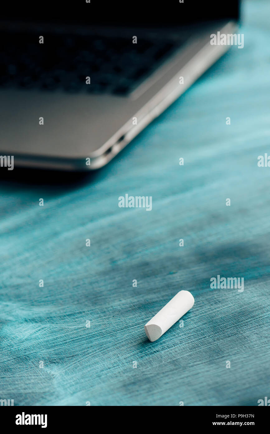 Piece of chalk on teacher's desk with laptop computer in the back Stock Photo