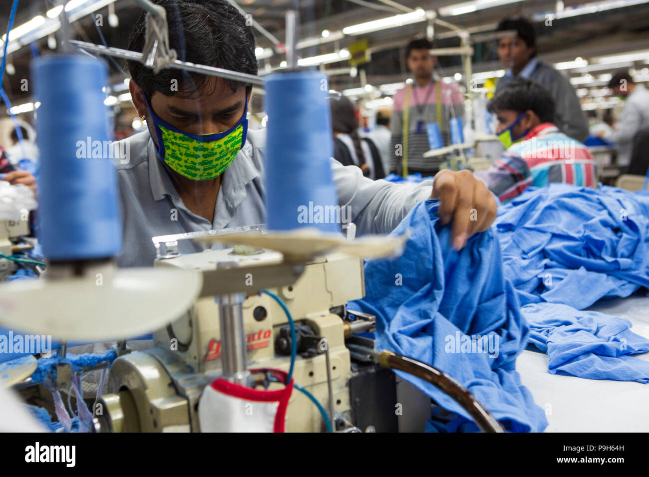 A man using a sewing machine on a production line of a garment factory, where organic cotton is being used to make clothes, Indore, India. Stock Photo
