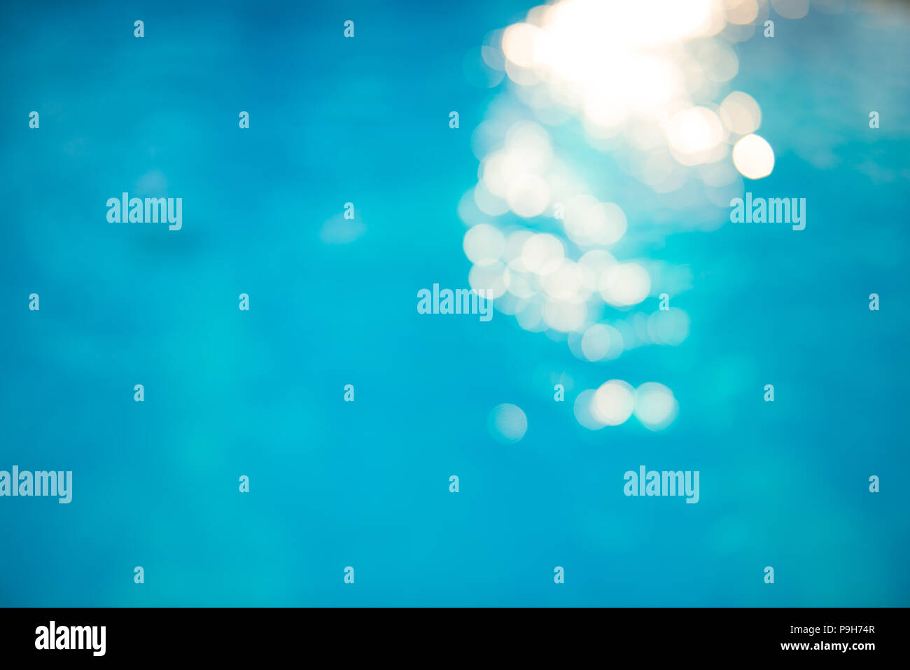Soft focus bokeh light effects over a rippled, blue water background in the pool. Stock Photo