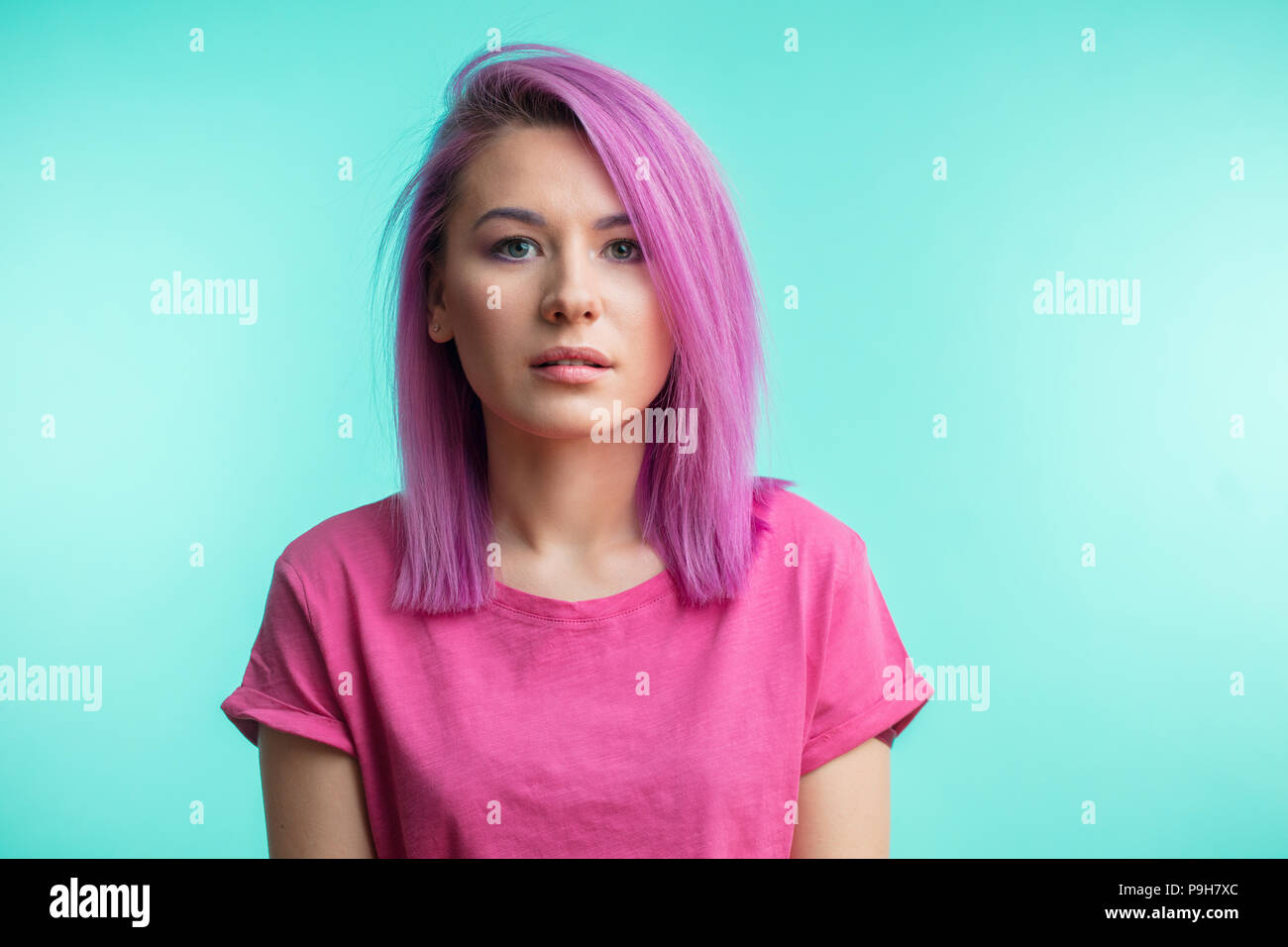 Head and shoulders portrait of caucasian young woman with pink hair, perfect fresh clean skin looking at camera with calm, serious expression over blu Stock Photo