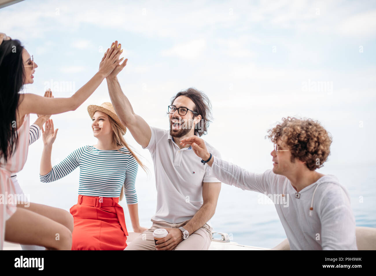 Happy cheerful young friends giving a high five slapping each others hand in congratulations, enjoying marine cruise on comfortable yacht Stock Photo