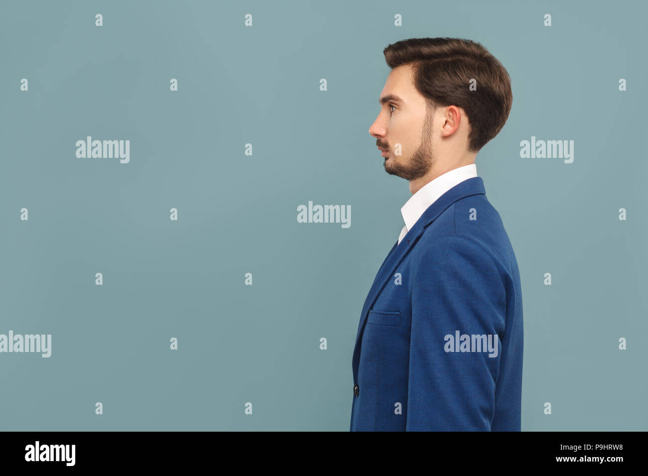 side view or profile view of serious handsome bearded businessman in blue suit and white shirt. Indoor studio shot, isolated on light blue background Stock Photo