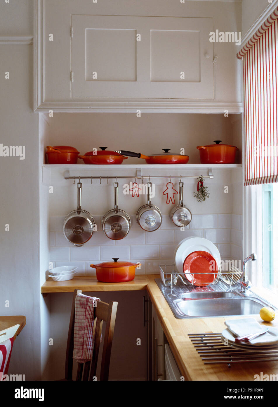 https://c8.alamy.com/comp/P9HRXN/row-of-orange-le-creuset-pans-on-shelf-above-stainless-steel-pans-on-rack-in-white-kitchen-P9HRXN.jpg