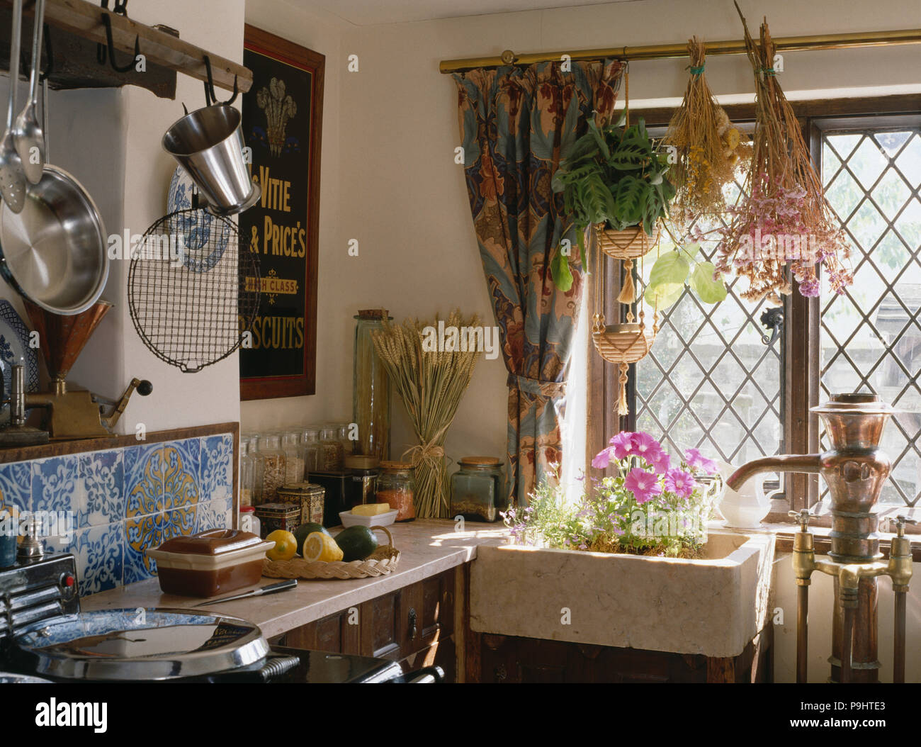 Dried flowers hanging above ceramic sink below lattice window in cottage kitchen Stock Photo