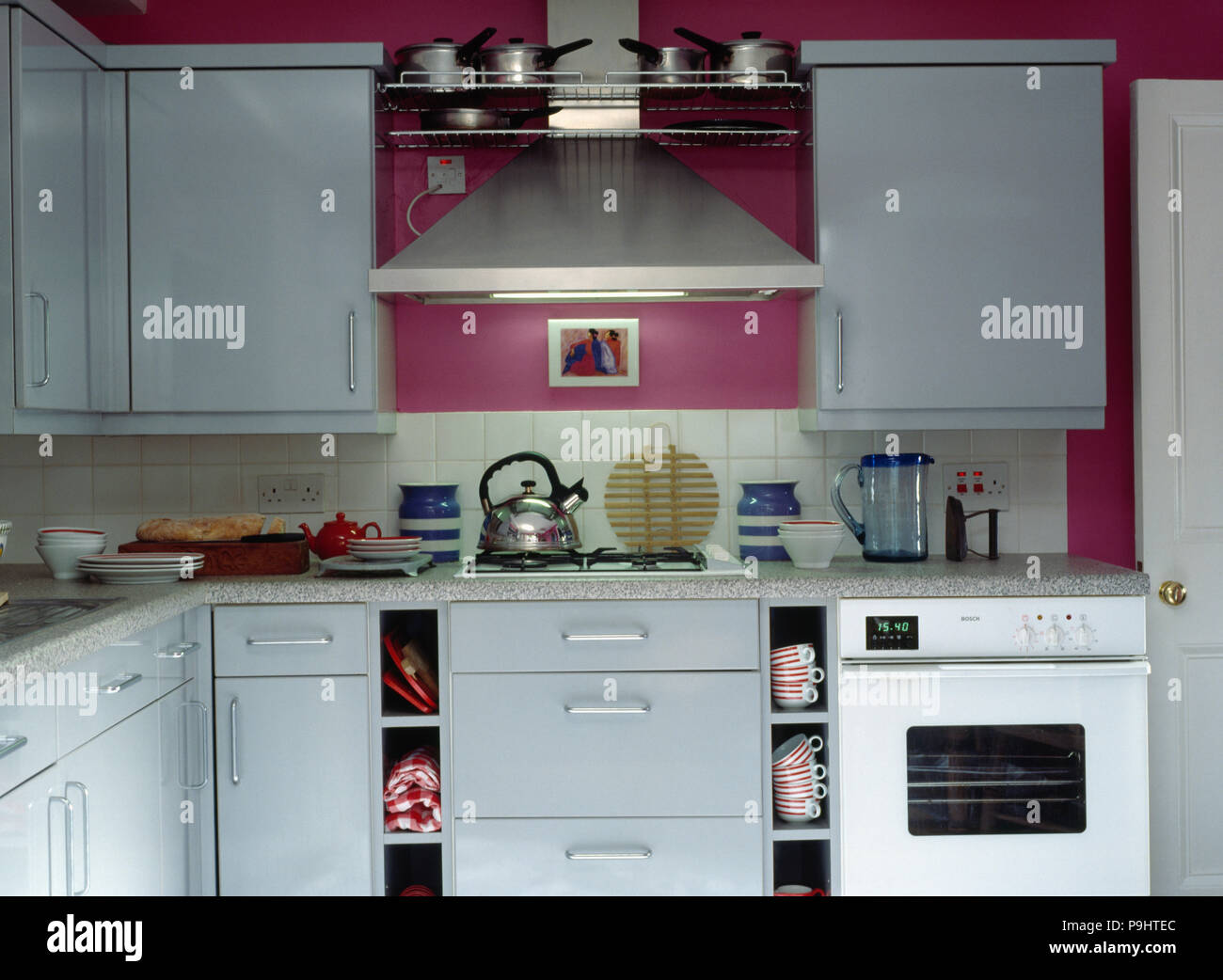 Stainless steel extractor above kettle on hob in small modern pink kitchen with fitted white units and white oven Stock Photo