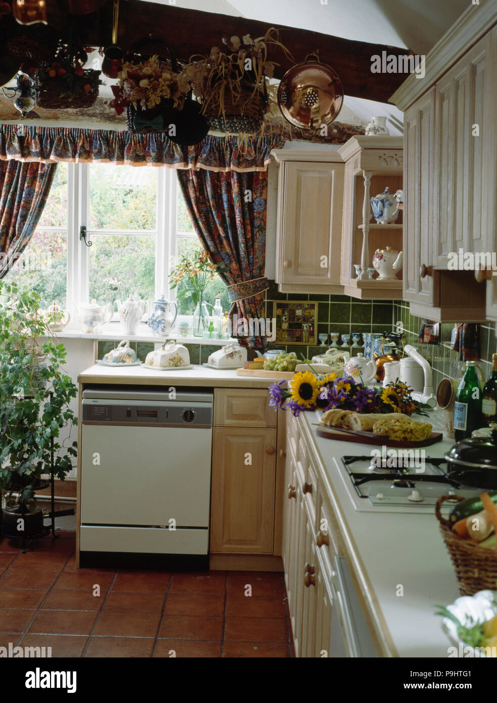 Fitted dishwasher below window in cluttered cottage kitchen Stock Photo