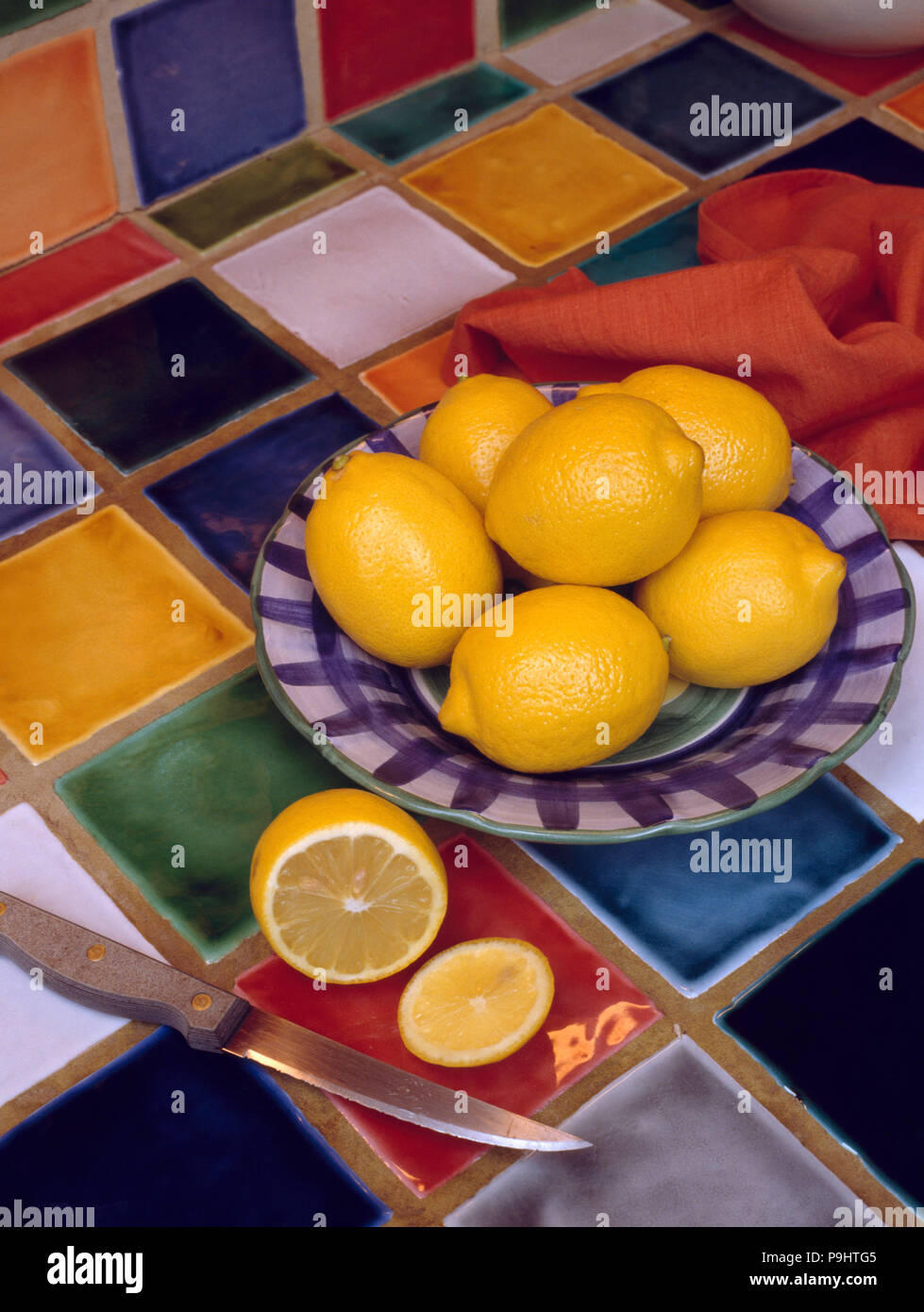 Yellow lemons on pottery plate on multi-coloured tiled worktop Stock Photo
